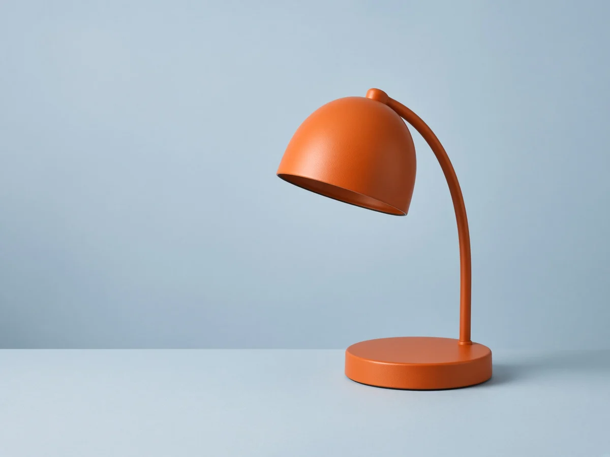 Orange dome desk lamp on a pale blue surface, with empty copy space to its left