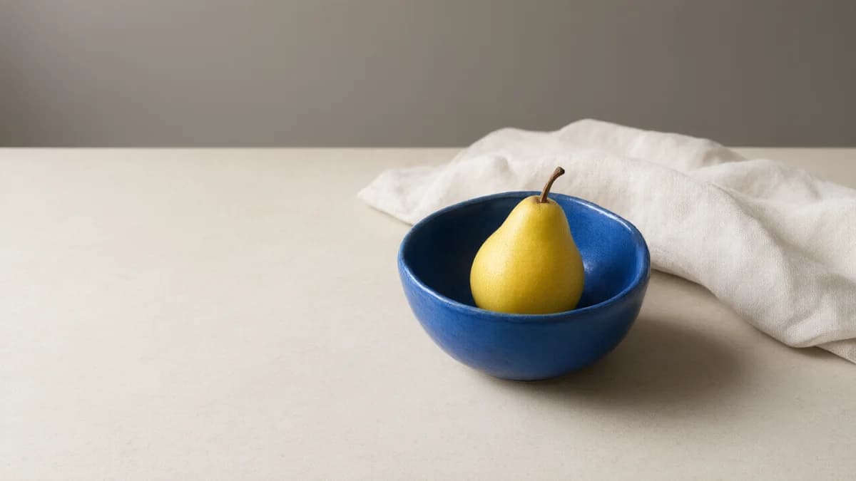 Reference image of a yellow pear in a blue bowl, with linen and open space to the left